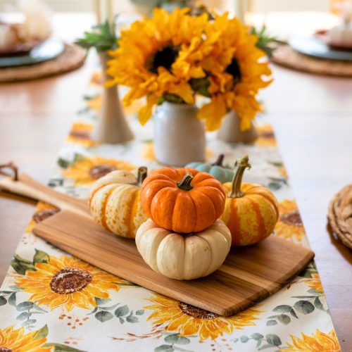 Assorted mini pumpkins on a wooden board with sunflower table runner and fall flowers for Thanksgiving decor.