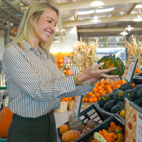 Woman in striped shirt selecting a green pumpkin from a colorful fall harvest market display.